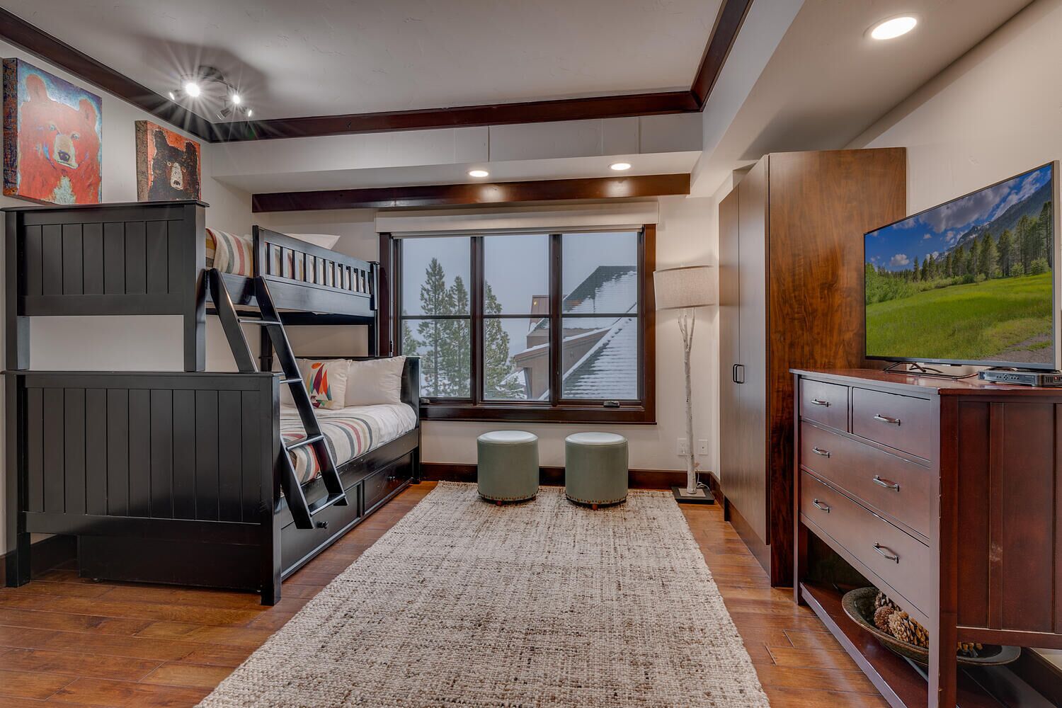 A room with bunk beds, a large window with a view, a TV, and a cabinet.