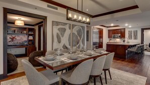 A dining area with a long table set for six, surrounded by six chairs. A kitchen is visible in the background. - Constellation #404 Ski-in & Out @ Northstar (Truckee)