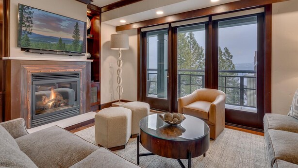 A living room with a fireplace, a television, and a large window with a view of trees. - Constellation #404 Ski-in & Out @ Northstar (Truckee)