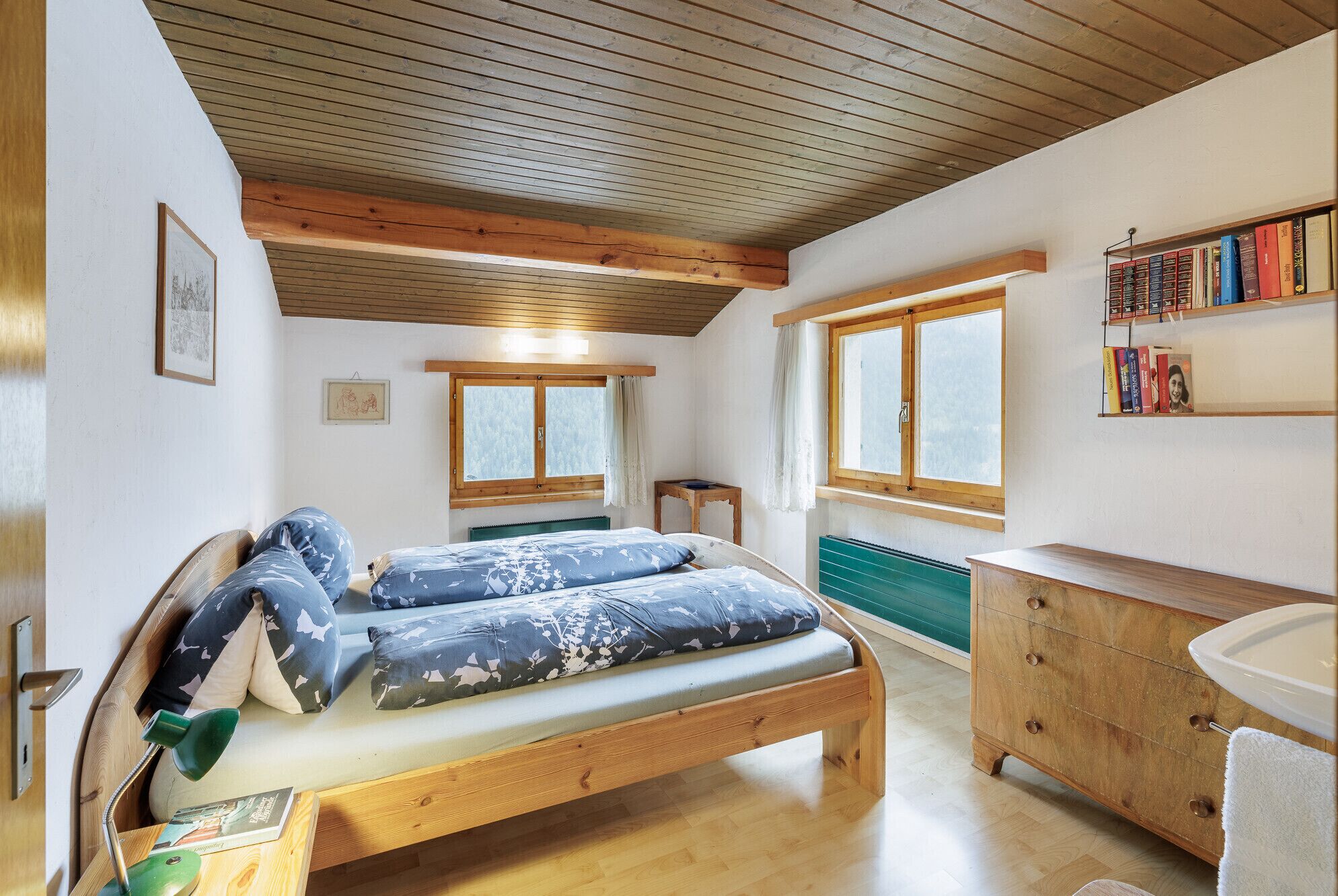 A bedroom with a wooden bed, a bedside table, a dresser, a window, and a bookshelf.