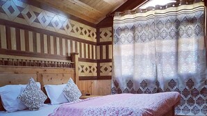 Una habitación de madera con una cama, cortinas estampadas y techo inclinado.