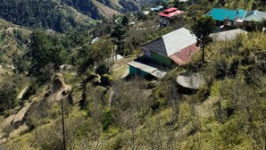 Un paisaje montañoso con un valle, casas con tejados de colores y un cielo azul despejado.