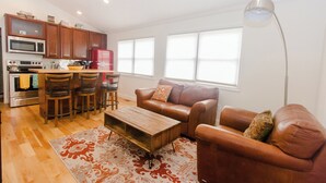 Una sala moderna con una mesa de centro de madera, sofás de cuero y una zona de cocina con armarios y electrodomésticos de madera.
