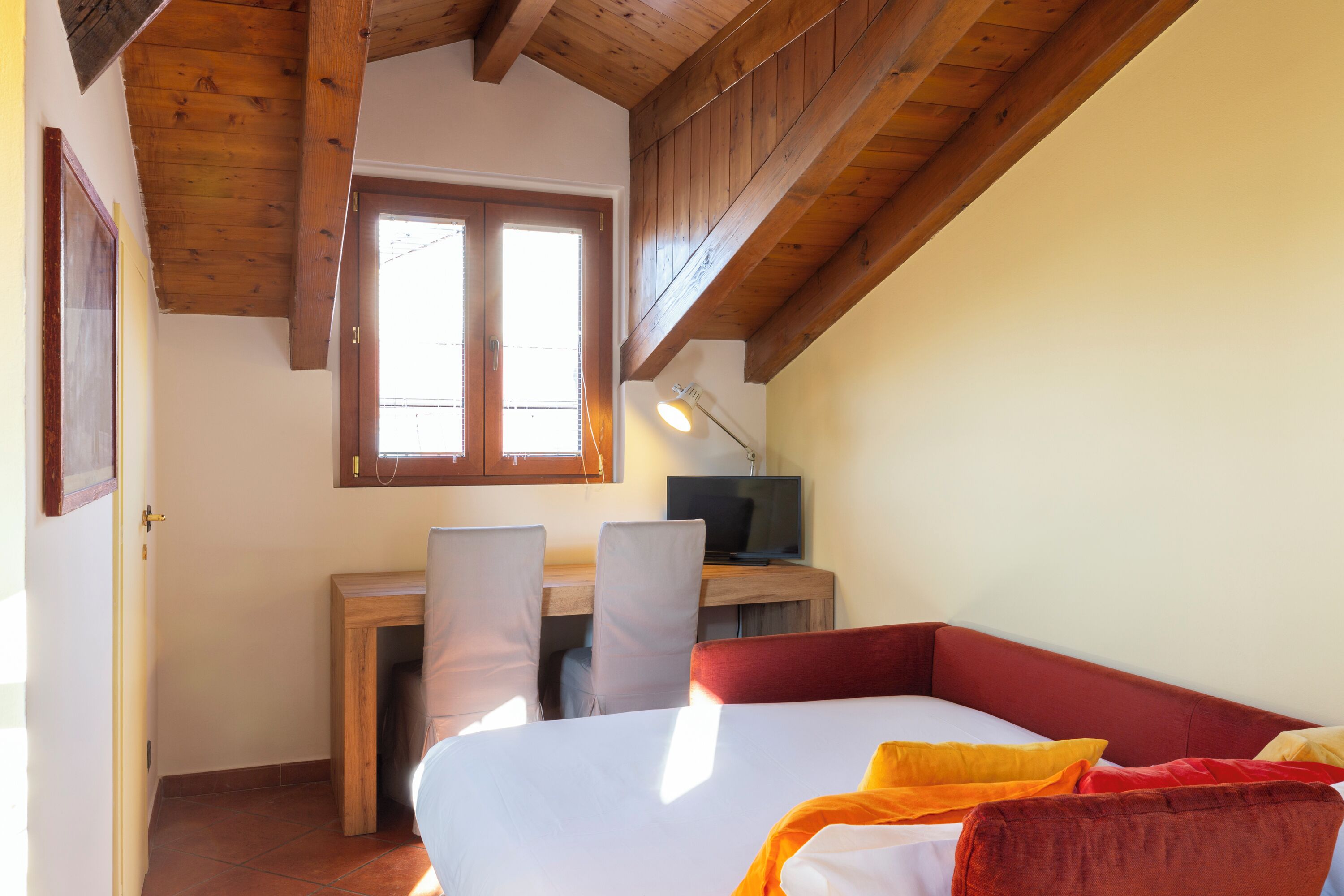 Une chambre avec un lit, un bureau et une chaise. Il y a une fenêtre au-dessus du bureau.