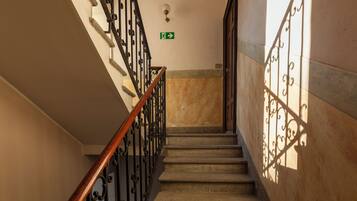 Una escalera con barandilla de madera y balaustradas de metal negro, que conduce a una plataforma con un letrero de salida de emergencia verde.