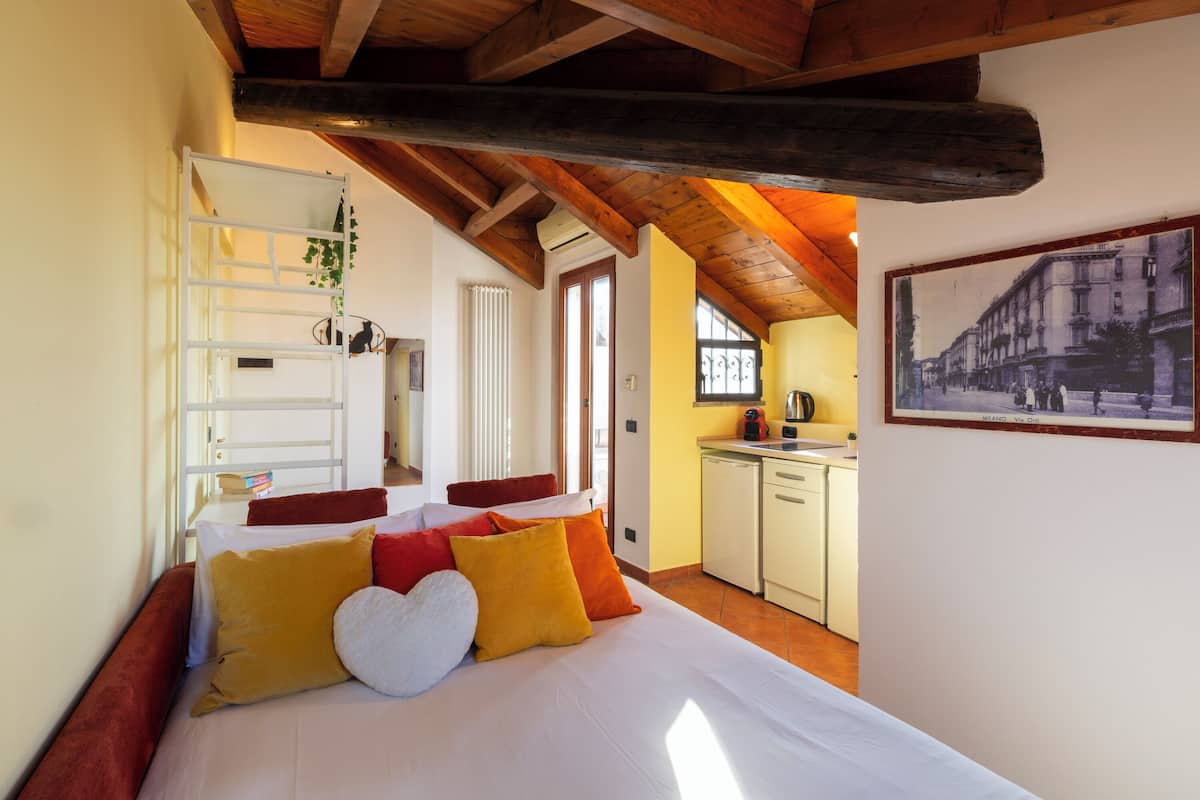 Un dormitorio con cama, almohadas, escritorio y kitchenette.