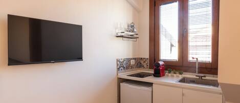 A compact kitchen with a built-in TV, a window with blinds, a sink, and a small countertop with a coffee maker.