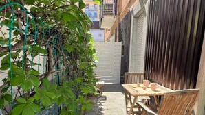 Eine schmale Außenpatio mit Tisch und Stühlen, einer Kletterpflanze und einem Holzzaun.