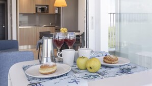 A breakfast setup with pastries, fruits, and a coffee maker on a table with a view of a balcony and a kitchen in the background. - Isaresidence three-room apartment Prestige Suite for 4 persons (Isolaverde di Chioggia)