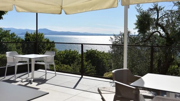 Une terrasse extérieure avec une table et des chaises, un parasol blanc et une vue sur la mer et les montagnes.