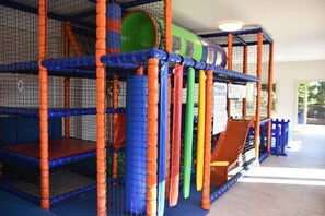 A multi-level indoor play area with netted walls and padded flooring.