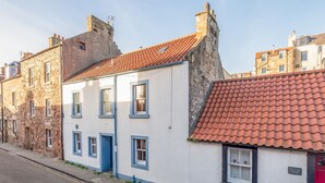 Un bâtiment traditionnel en pierre, doté d’une façade blanche et de bordures bleues, avec un toit recouvert de tuiles rouges et une petite fenêtre agrémentée de volets.
