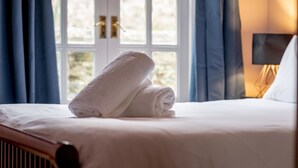 Un lit bien fait, avec une serviette blanche pliée, une fenêtre ornée de rideaux bleus et une lampe de chevet.