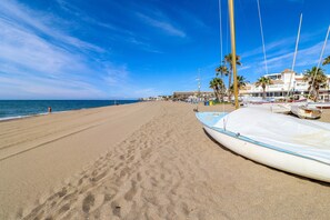 A beach with a row of boats, palm trees, and a building in the background. - La Cala beach apartment (La Cala de Mijas)