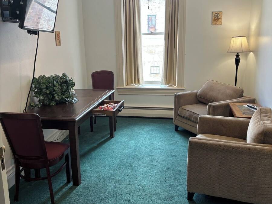 A hotel room with a dining table, two chairs, a sofa, a TV, a lamp, and a window with curtains.