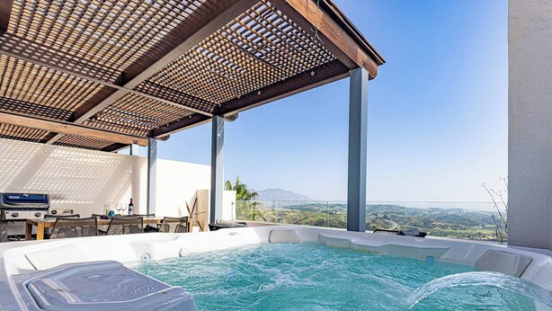 Un jacuzzi con un techo de madera, una mesa con sillas y vistas del paisaje.