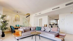 Una sala de estar moderna con un sofá seccional, una mesa de centro de madera y una escalera que conduce a un nivel superior.
