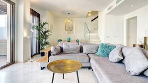 Una sala moderna con un sofá modular, una mesa de centro y una escalera al fondo.