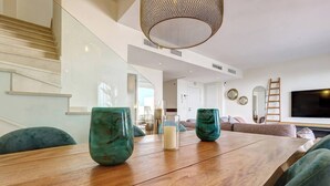 Una sala moderna con una mesa de comedor de madera, jarrones verde azulado y un televisor grande.