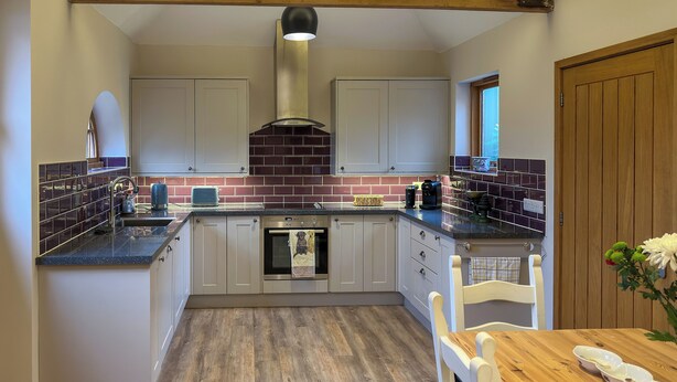 Una cocina con vigas de madera, salpicadero de ladrillo y una mesa de comedor de madera con cuencos.