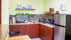 A compact kitchen with wooden cabinets, a stainless steel refrigerator, a microwave, and a tiled backsplash.