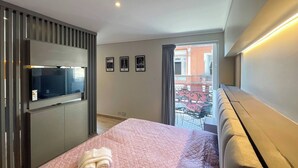 Une chambre d’hôtel moderne équipée d’un lit, d’un téléviseur à écran plat, d’un balcon offrant une vue sur les bâtiments et d’un téléviseur fixé au mur.