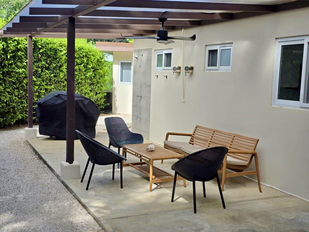 An outdoor patio with a wooden table and chairs, a barbecue grill, and a pergola with a ceiling fan.