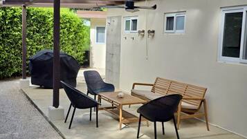 An outdoor patio with a wooden table and chairs, a barbecue grill, and a pergola with a ceiling fan.