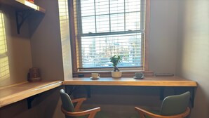 A small, cozy workspace with a wooden desk, two green chairs, a potted plant, and a window with blinds. - NEW! Modern Private Entrance, 2BD Apt. Minutes to NYC (Jersey City)