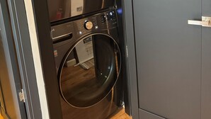 A laundry room with two washing machines and a dryer, a brick wall, and a wooden floor. - NEW! Modern Private Entrance, 2BD Apt. Minutes to NYC (Jersey City)