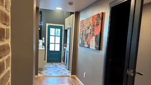 A hallway with wooden flooring, a rug, a door, and a wall with a colorful abstract painting. - NEW! Modern Private Entrance, 2BD Apt. Minutes to NYC (Jersey City)