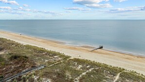 Une plage avec un rivage sablonneux, un petit quai et une zone herbeuse bordée d’une rambarde métallique.