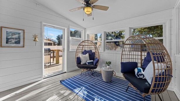 Une pièce baignée de lumière, avec un ventilateur de plafond, deux fauteuils en osier dotés de coussins, un tapis à rayures et une petite table sur laquelle est posée une plante.