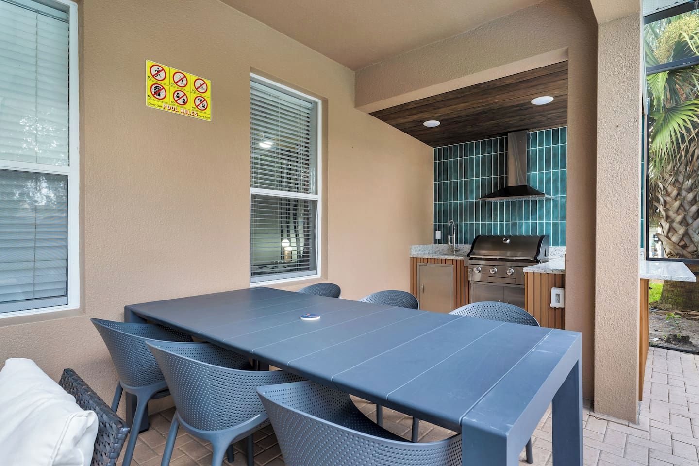 An outdoor dining area with a table and chairs, a grill, and a window with blinds.