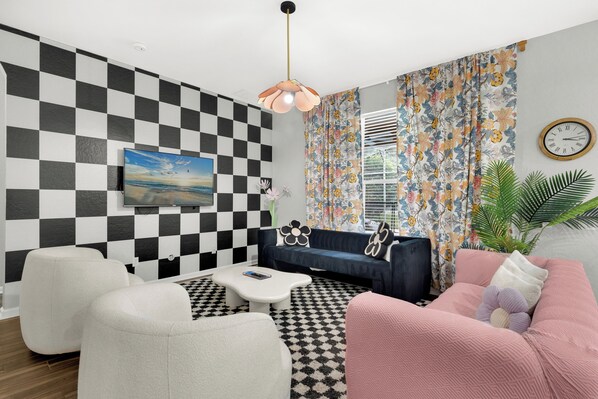 A modern living room with a checkered wall, a flat-screen TV, a sofa, a coffee table, and a patterned curtain.
