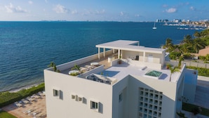A modern building with a rooftop terrace overlooking a body of water, featuring sun loungers and a pool. - Villa Punta Sam Cancun Beachfront Luxury (Cancun)