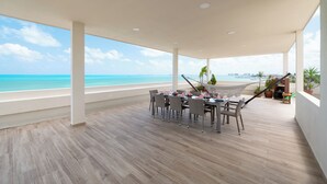 A spacious outdoor area with a dining table and chairs, a hammock, and a view of the ocean. - Villa Punta Sam Cancun Beachfront Luxury (Cancun)