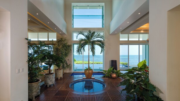A spacious indoor area with a pool, large windows, and potted plants. - Villa Punta Sam Cancun Beachfront Luxury (Cancun)