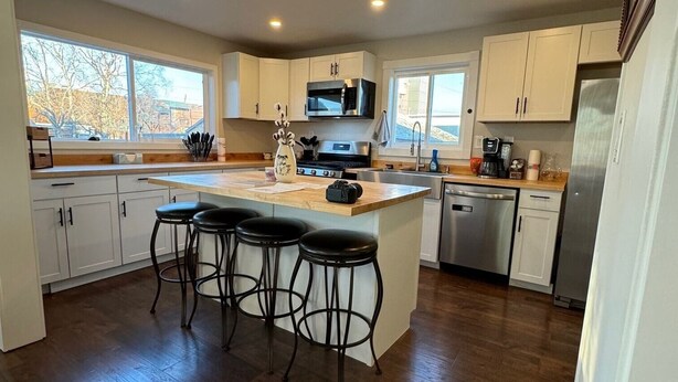 A modern kitchen with white cabinets, a central island with bar stools, stainless steel appliances, and large windows providing natural light. - Newly Remodeled Charming Cozy 3-bedroom house in Anchorage with WiFi (Anchorage)