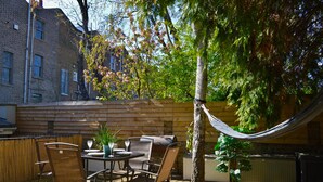 An outdoor patio with a wooden table and chairs, a hammock, and a potted plant.