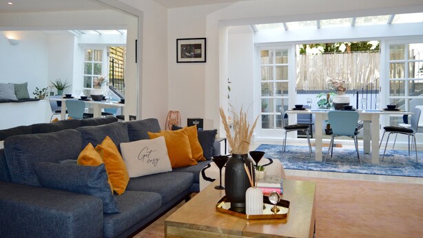 A modern living room with a grey sofa, a coffee table, and a dining area with a white table and chairs.