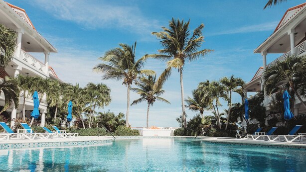 Una piscina con agua azul cristalina, rodeada de palmeras y sillas de descanso azules.