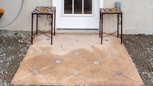 A white door with a decorative tile border, two small tables with patterned tiles, and a concrete patio with decorative tiles. - Casita Talavera (Nashville)