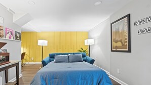 A bedroom with a large bed, a desk, and a chair. There is a yellow wall and a framed picture on the wall. - Casita Talavera (Nashville)