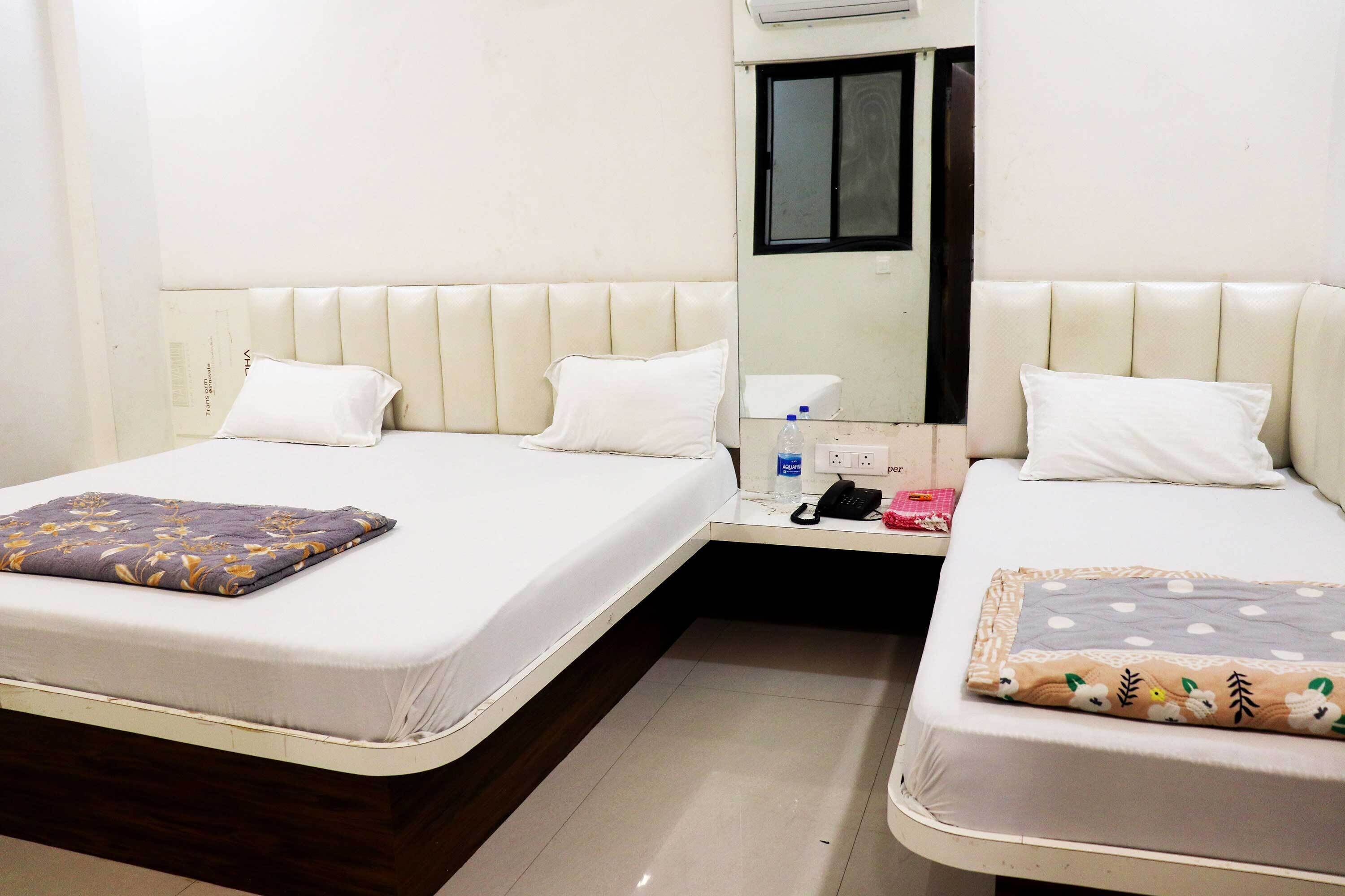 Habitación de hotel con dos camas, cada una con una almohada y una manta. Hay una mesita con un teléfono y una botella de agua.