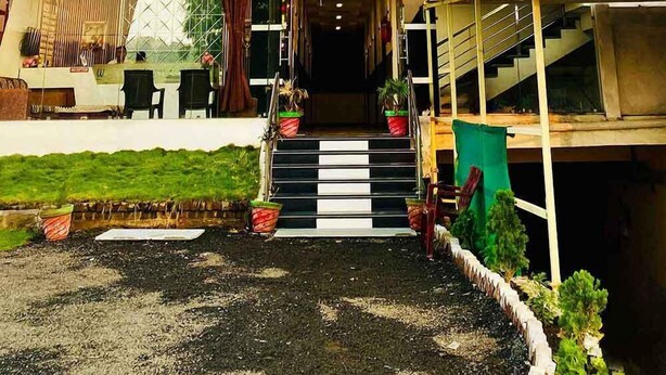 Hotel anomenat "Hotel Gayatri Palace" amb una gran façana de vidre blau, una escala que condueix a l'entrada i una petita zona de jardí amb plantes en testos.