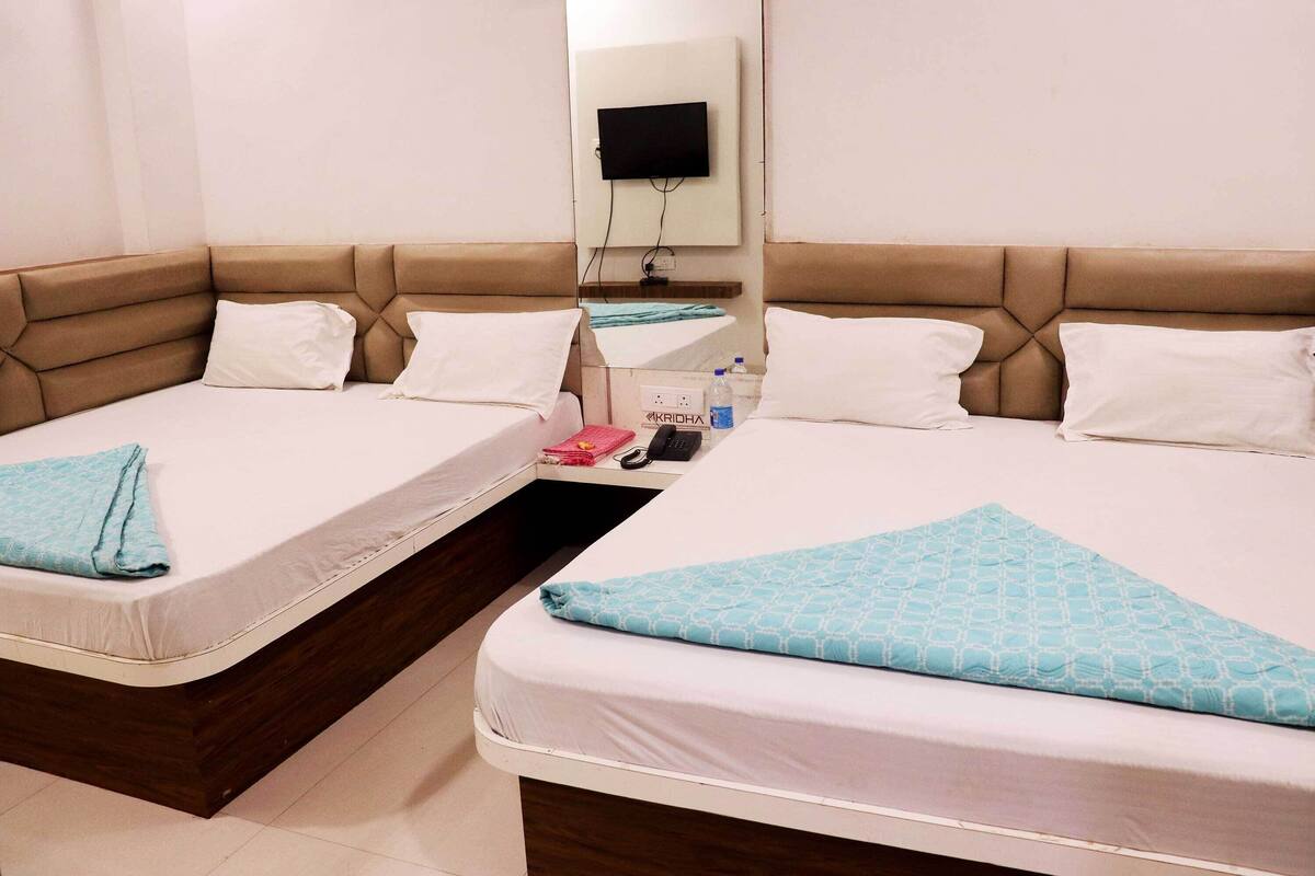 A hotel room with two beds, a TV mounted on the wall, a bedside table with a phone and a water bottle, and a small mirror.