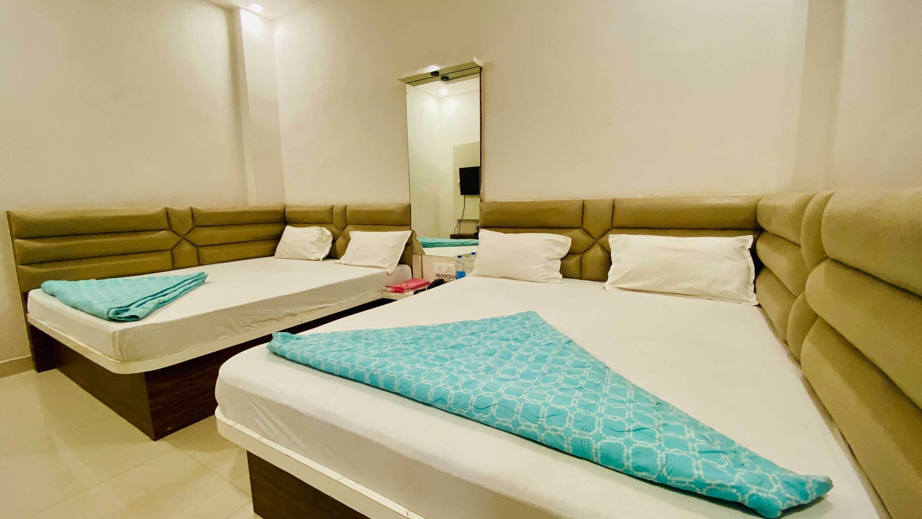 A hotel room with two beds, a large mirror, and a bedside table with a bottle.
