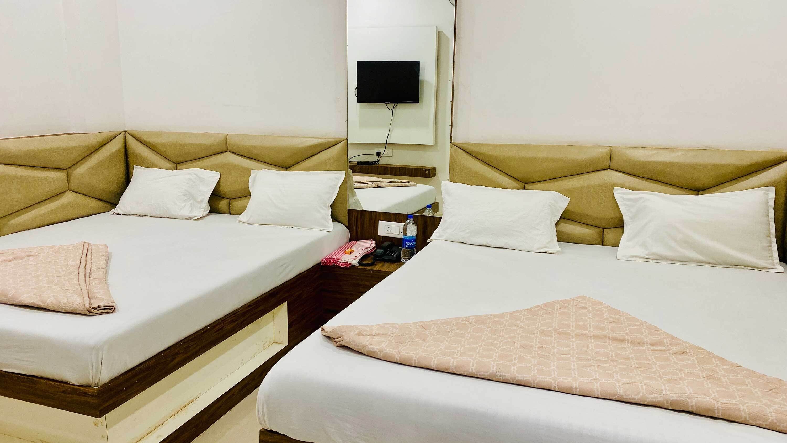 Une chambre d’hôtel avec deux lits, un téléviseur fixé au mur, une table de chevet avec un téléphone et une bouteille d’eau, et un miroir au-dessus de la table.