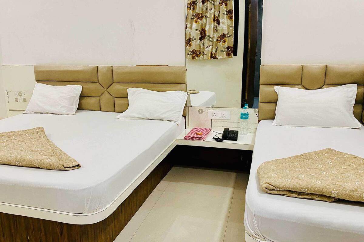A hotel room with two beds, each with a beige headboard and white bedding. There is a small table between the beds with a water bottle, a phone, and a folded towel.